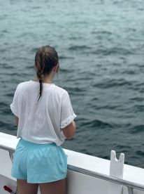 A young angler is focused on fishing from the side of a boat, casting into the open water, showcasing the excitement of a fishing adventure.