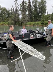 A family enjoying a fishing trip on a riverboat, with kids preparing gear and a scenic backdrop of trees.
