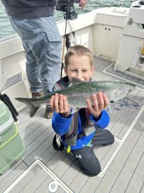 A young angler proudly displaying a caught fish while kneeling on the deck of a fishing boat.