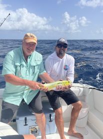 Two anglers proudly displaying a vibrant Mahi-Mahi while fishing offshore, showcasing a sunny day on the water.