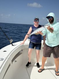 Two anglers proudly displaying a large Barracuda while fishing offshore, showcasing a successful day on the water.