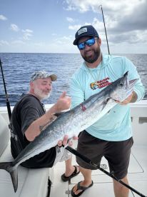 Two anglers proudly displaying a large King Mackerel aboard a fishing charter in open waters.