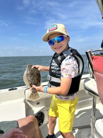 A young angler proudly displaying a Flounder while enjoying a sunny day on the water.