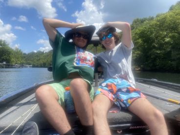 Two young anglers enjoying a sunny day on a fishing boat, showcasing a relaxed atmosphere on a lake.