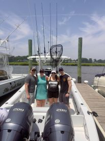 A group of four friends posing on the deck of a fishing boat, showcasing the boat's interior and fishing gear setup.