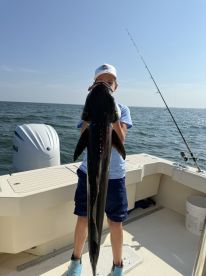 A young angler proudly displaying a large Cobia on a fishing boat, showcasing a successful day on the water.