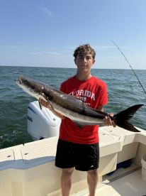 A young angler proudly displaying a large Cobia while fishing on a boat in open waters.