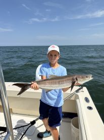 Young angler proudly holding a Cobia while fishing on a boat in open waters.