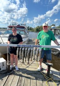 Two anglers proudly displaying their catch of multiple trout on a board at the dock, showcasing a successful fishing trip with King's Sportfishing Adventures.
