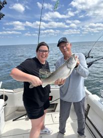 Two anglers proudly displaying a large Lake Trout on a fishing boat, enjoying a sunny day on the water.