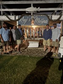 Group of anglers posing in front of a catch board displaying several fish at Ray's Marina, showcasing their successful fishing trip.