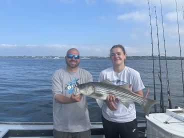 A young angler and an adult proudly displaying a large Striped Bass while fishing on a calm day.