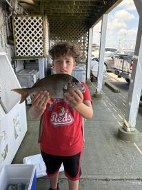 A young angler proudly displaying a freshly caught fish at the dock, showcasing the excitement of a fishing trip.