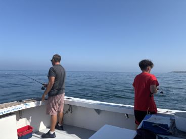 A father and son enjoying a fishing trip on a boat, casting their lines into calm waters under a clear blue sky.