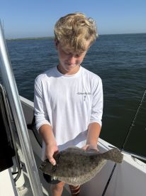 A young angler holding a Flounder on a fishing boat, showcasing a successful catch during a sunny day on the water.