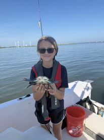 A young angler proudly holding a blue crab while fishing on a boat, showcasing a fun day on the water.