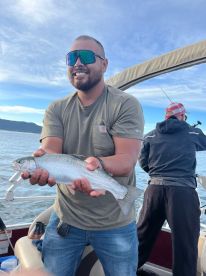 An angler proudly displaying a Rainbow Trout while fishing on a boat, showcasing a beautiful day on the water.