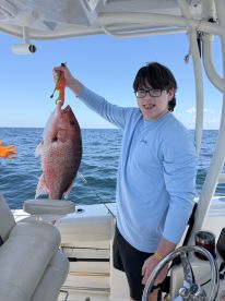 A young angler proudly displaying a large Snapper while fishing on a boat in open waters.