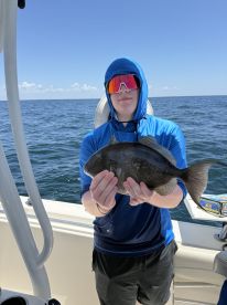 A young angler proudly displaying a Black Sea Bass while fishing offshore, showcasing a sunny day on the water.