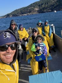 A cheerful group of anglers, including a child in a life jacket, enjoying a fishing trip aboard a small boat, surrounded by scenic coastal views.