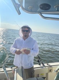 Angler holding a small fish while fishing on a boat in calm waters, showcasing a relaxed day on the water.