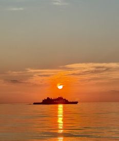 A serene sunset view featuring a fishing boat silhouetted against the vibrant orange sky, reflecting on calm waters.