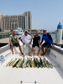 A group of four anglers proudly displaying their catch of Mahi Mahi on the deck of a sportfishing boat, with a marina backdrop.