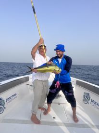 Two anglers proudly displaying a vibrant Mahi Mahi aboard a sportfishing boat in open waters.