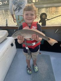 A young angler proudly displaying a Redfish while fishing on a boat, showcasing a fun family fishing experience.
