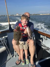 A young angler proudly displaying a Flounder and a Snapper while seated on a boat, enjoying a fishing adventure.