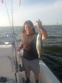 An angler proudly displaying a large Speckled Trout while fishing on a boat in coastal waters.