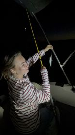 A young angler joyfully holding up a small fish while fishing at night, showcasing the excitement of night fishing.