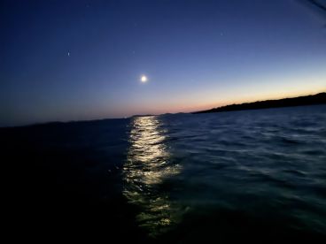 A serene twilight scene over the water, showcasing the moon's reflection on the surface, ideal for evening fishing trips.