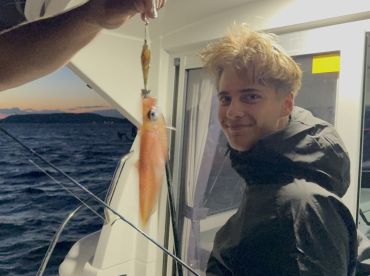 A young angler smiling while holding a freshly caught squid aboard a fishing boat during a sunset trip.