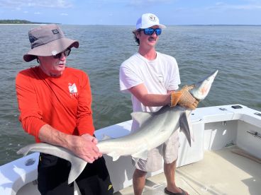 Two anglers proudly displaying a large shark while fishing on a boat in coastal waters.