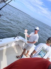 Angler proudly displaying a freshly caught fish aboard a fishing boat in a coastal waterway.