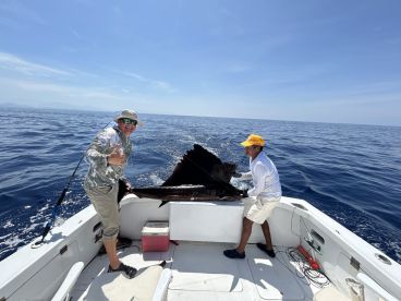 Two anglers actively reeling in a large fish while enjoying a sunny day on the open ocean.