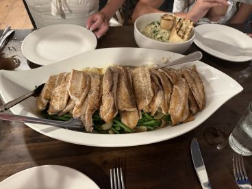 A plate of cooked fish fillets served with green beans and mashed potatoes, set on a dining table with additional dishes in the background.