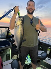An angler proudly displaying a large Salmon while aboard a fishing boat during sunset.