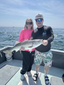 Two anglers proudly displaying a large Striped Bass aboard a boat during a fishing trip off Cape Cod.