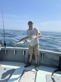 Angler proudly displaying a large Striped Bass while fishing on a boat in open waters.