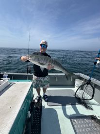 Angler displaying a large Striped Bass aboard a fishing boat, showcasing a successful day on the water.
