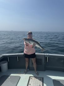 An angler proudly displaying a large Striped Bass while fishing on a boat in clear waters.