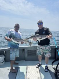 Two anglers proudly displaying their striped bass catch while fishing on a boat in open waters.