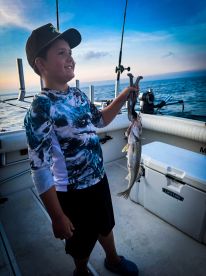 A young angler proudly displaying a caught fish while fishing on a boat during a beautiful sunset.