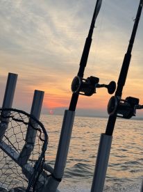A scenic view from a fishing boat at sunset, featuring fishing rods and a net against the backdrop of the ocean.