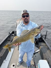 Angler proudly displaying a Walleye while fishing on a boat in open water.