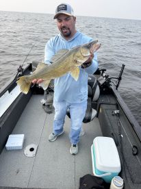 An angler proudly displaying a large Walleye while fishing on a boat, showcasing a successful day on the water.