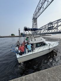 A group of anglers aboard a fishing boat navigating under a bridge, showcasing a scenic waterfront environment.