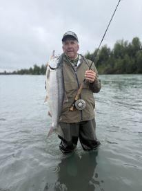 An angler proudly displaying a large Silver Salmon while wading in a river, showcasing the thrill of freshwater fishing.